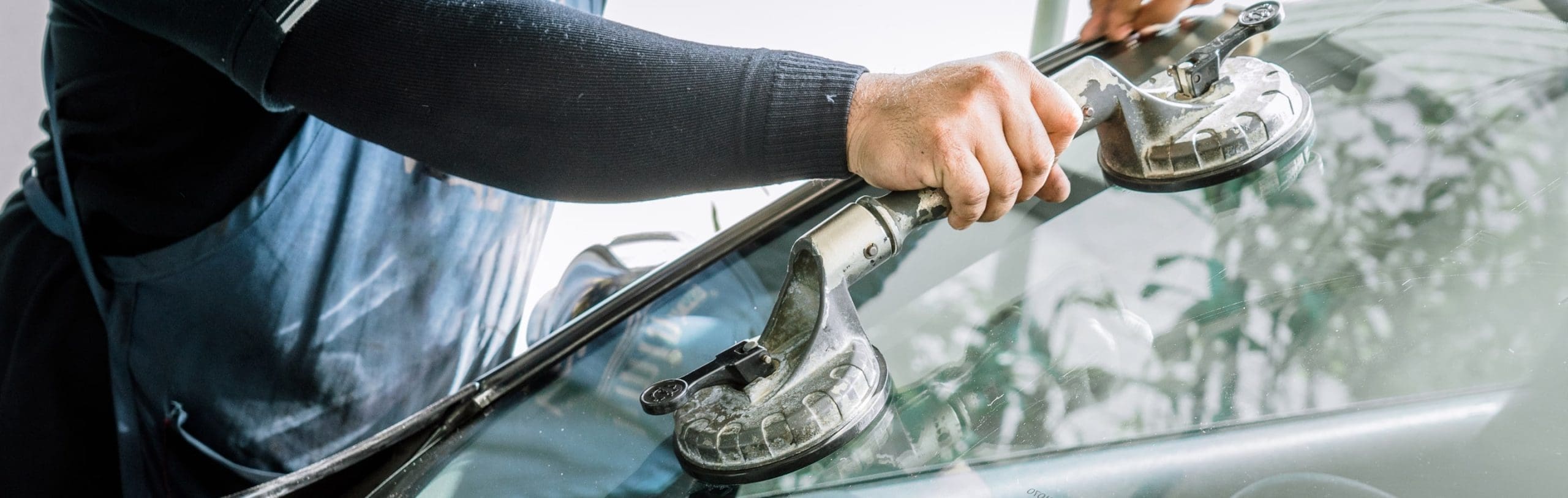 Auto glass technician using suction cups to install or repair windshield, showcasing professional automotive glass services related to Prime Auto Glass & Tint.